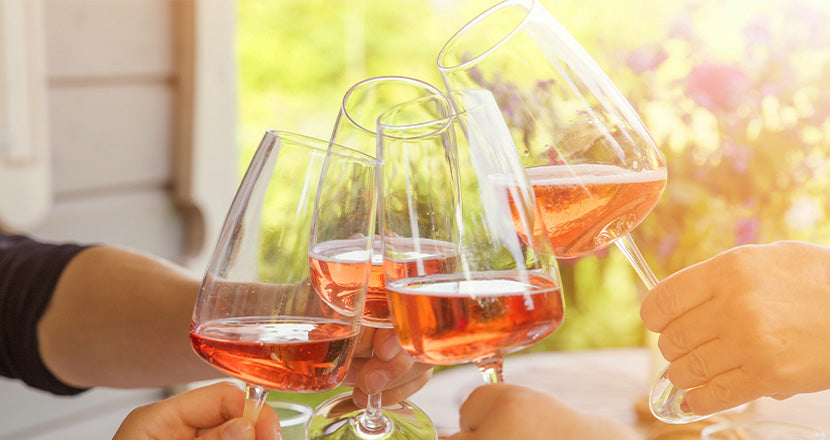 Vier Menschen stoßen mit Gläsern Roséwein in der warmen Nachmittagssonne an